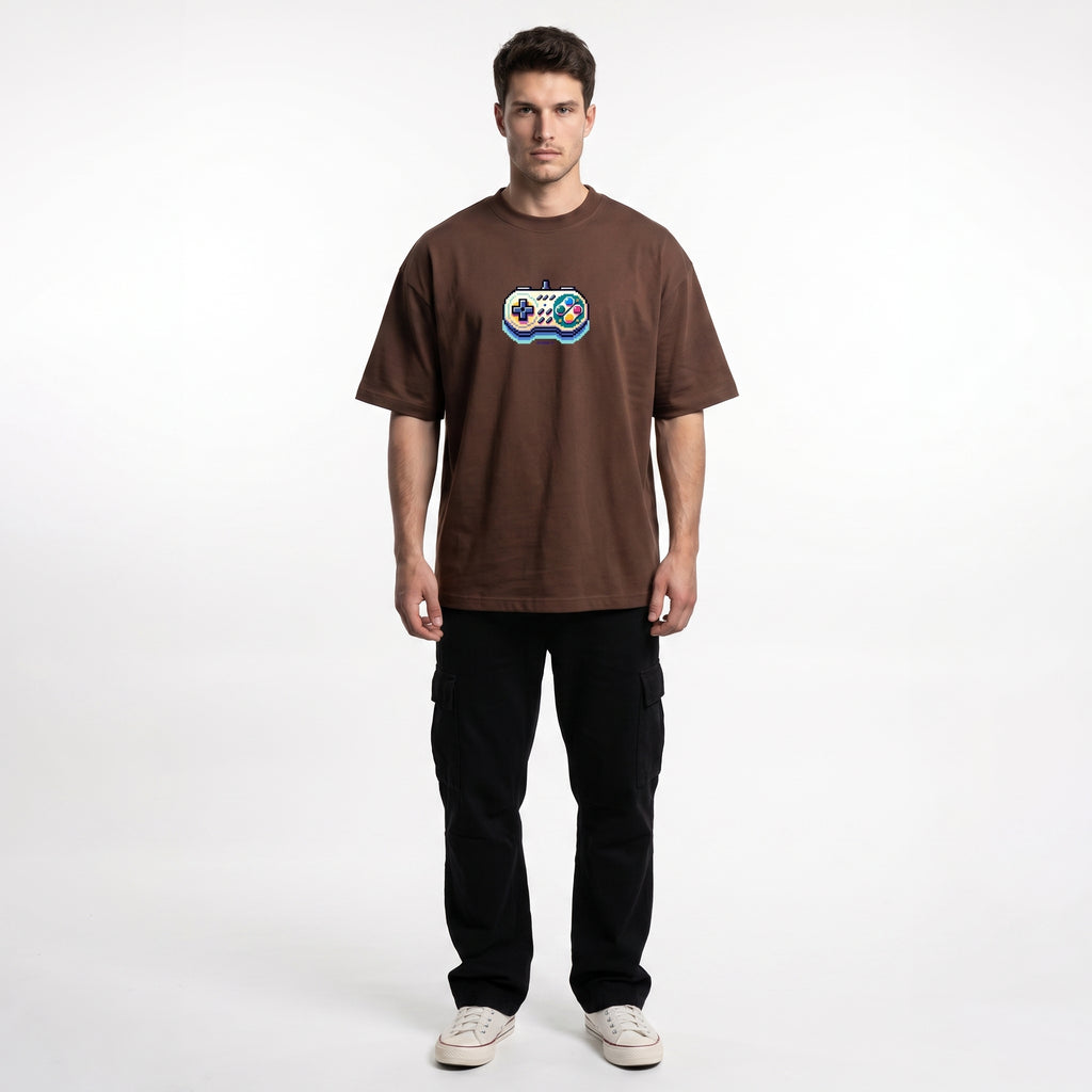 A man modeling a brown short-sleeve t-shirt with a colorful graphic on the chest, paired with black cargo pants and white sneakers, against a plain white studio background.