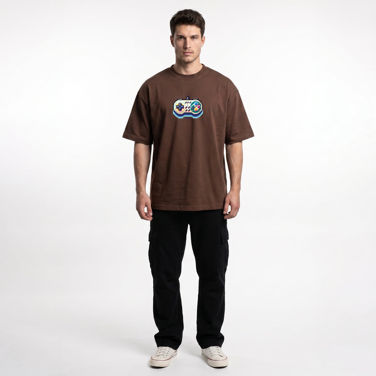 A man modeling a brown short-sleeve t-shirt with a colorful graphic on the chest, paired with black cargo pants and white sneakers, against a plain white studio background.