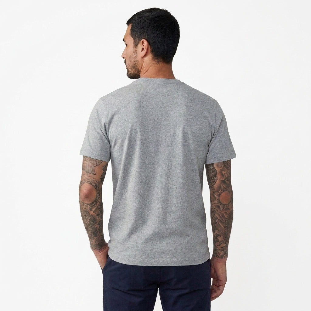 A man with tattoos is shown from the back wearing a light gray heather crewneck t-shirt and dark navy pants, photographed against a clean white background.