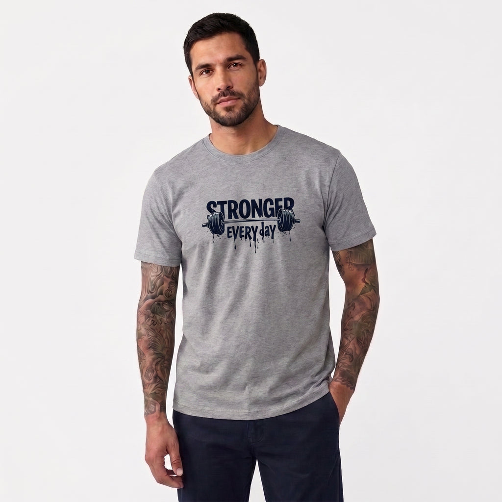 A man wearing a heather gray crewneck t-shirt with a black graphic print that reads 'STRONGER EVERY DAY' with a barbell design, set against a plain light gray background.