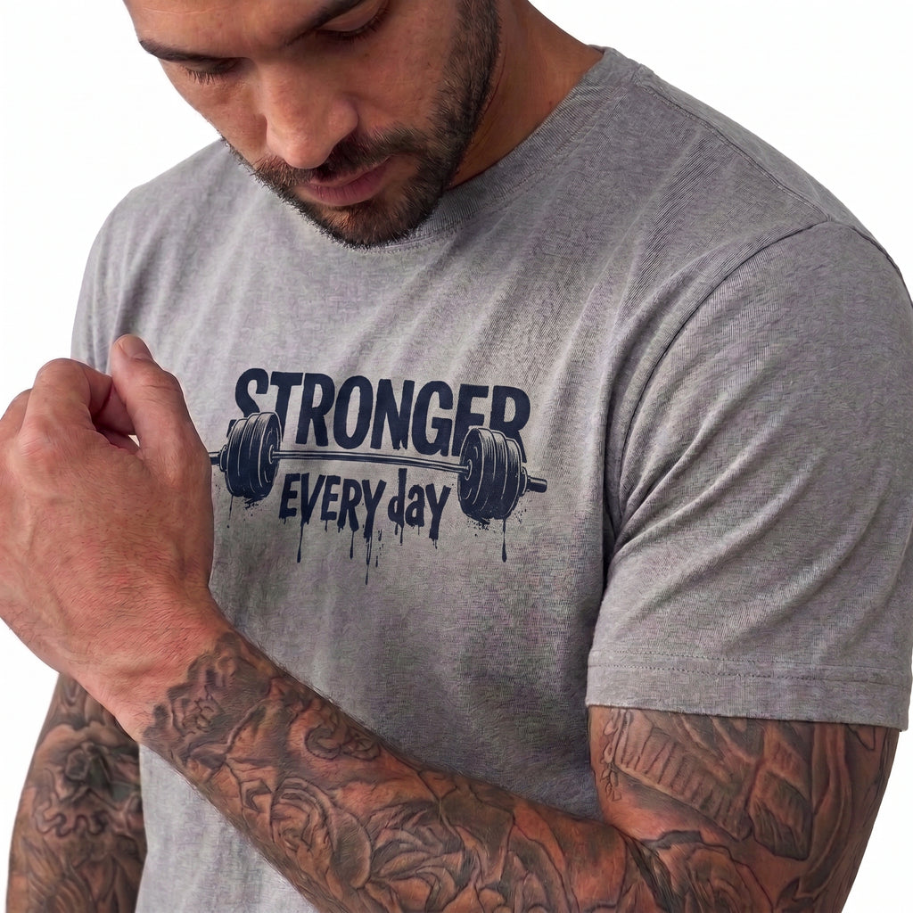 A close-up of a man wearing a heather gray t-shirt with a dark navy graphic that reads 'STRONGER EVERY day' with a barbell design, set against a plain white background.