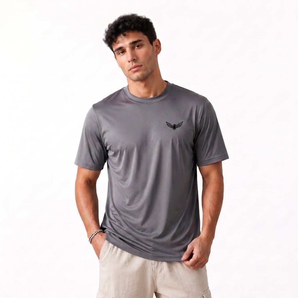 A man wearing a dark gray short-sleeve athletic t-shirt with a small black winged logo on the left chest, paired with beige shorts, photographed against a clean white background.