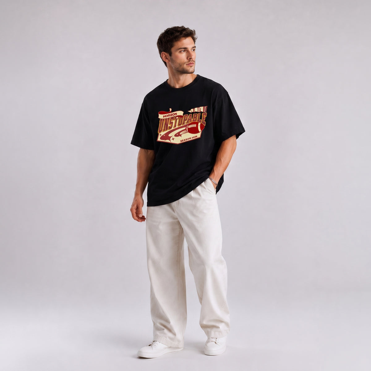 A man modeling a black t-shirt with a red and gold graphic print that reads 'MEXICO', paired with off-white trousers and white sneakers, set against a plain light gray studio background.
