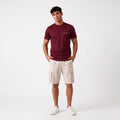 A man modeling a burgundy short-sleeve t-shirt with a small white 'HERR&WEISE' logo on the chest, paired with beige cargo shorts and white sneakers, against a plain white studio background.