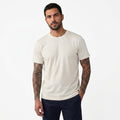 A man with tattoos modeling a plain off-white crewneck t-shirt and dark navy pants against a clean white background.