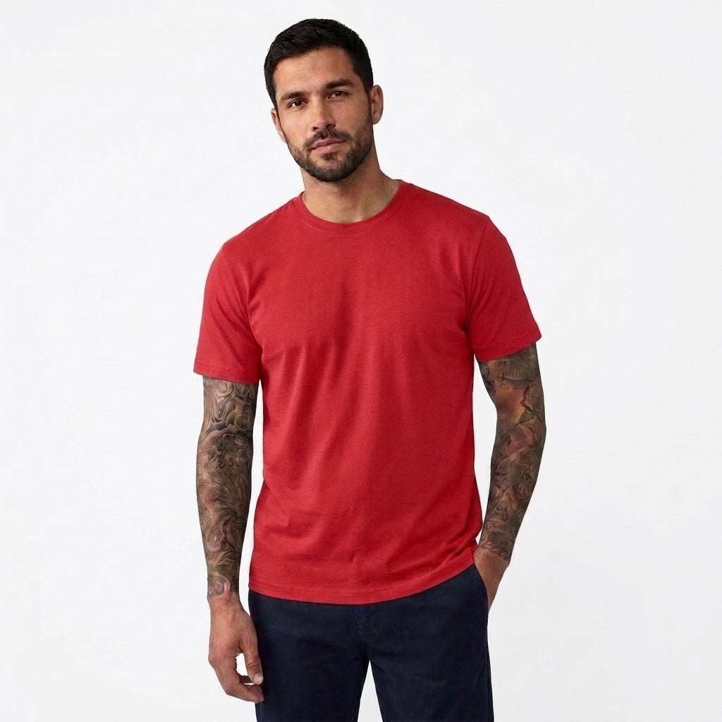 A man wearing a solid red crew-neck t-shirt and dark navy pants, standing against a plain white studio background.
