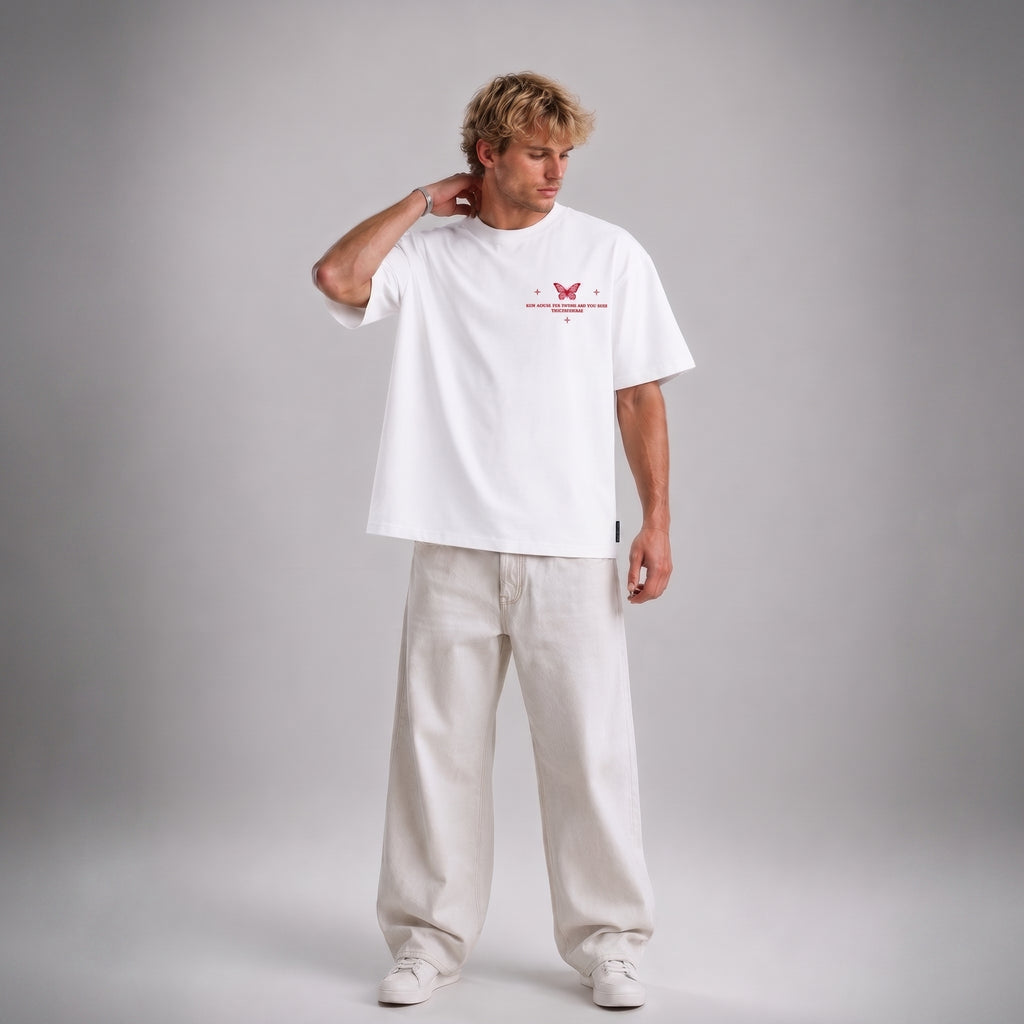A man modeling a white short-sleeve t-shirt with a red butterfly graphic and text on the chest, paired with off-white wide-leg trousers, against a neutral gray studio background.