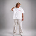 A man modeling a white short-sleeve t-shirt with a red butterfly graphic and text on the chest, paired with off-white wide-leg trousers, against a neutral gray studio background.