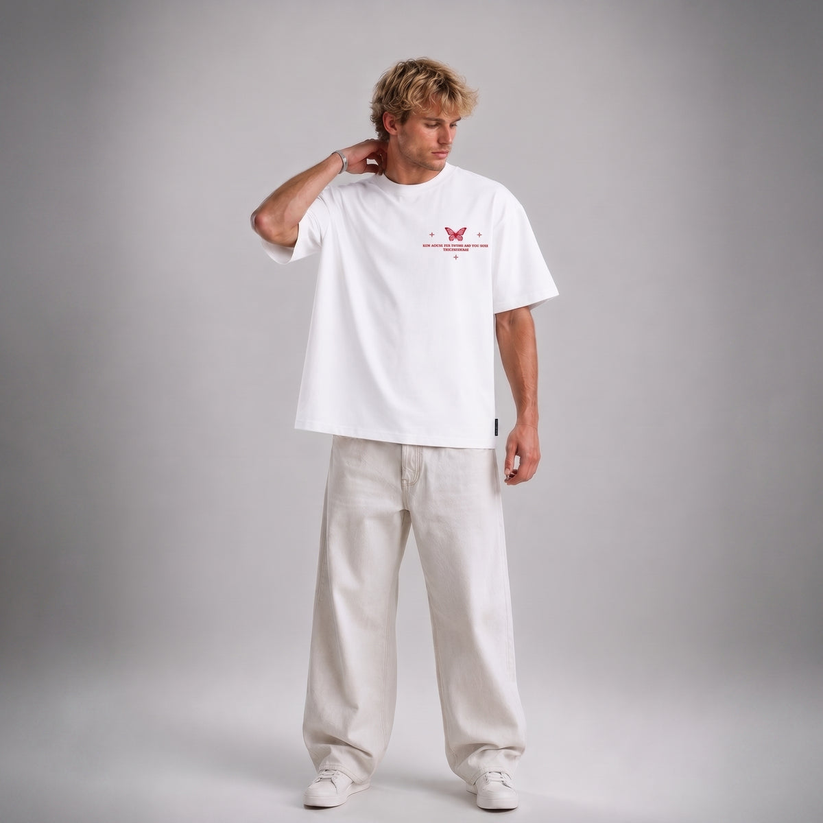 A man modeling a white short-sleeve t-shirt with a red butterfly graphic and text on the chest, paired with off-white wide-leg trousers, against a neutral gray studio background.